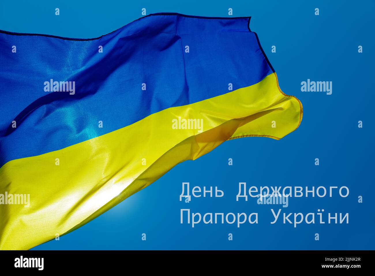 la bandera ucraniana volando en el cielo en un día soleado, y el texto bandera día de ucrania escrito en ucraniano Foto de stock