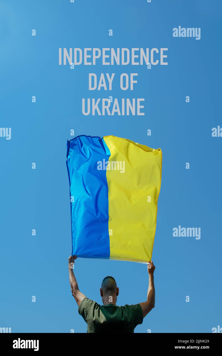 texto día de la independencia de ucrania y un hombre, visto desde atrás, agitando la bandera ucraniana sobre el cielo por encima de su cabeza Foto de stock