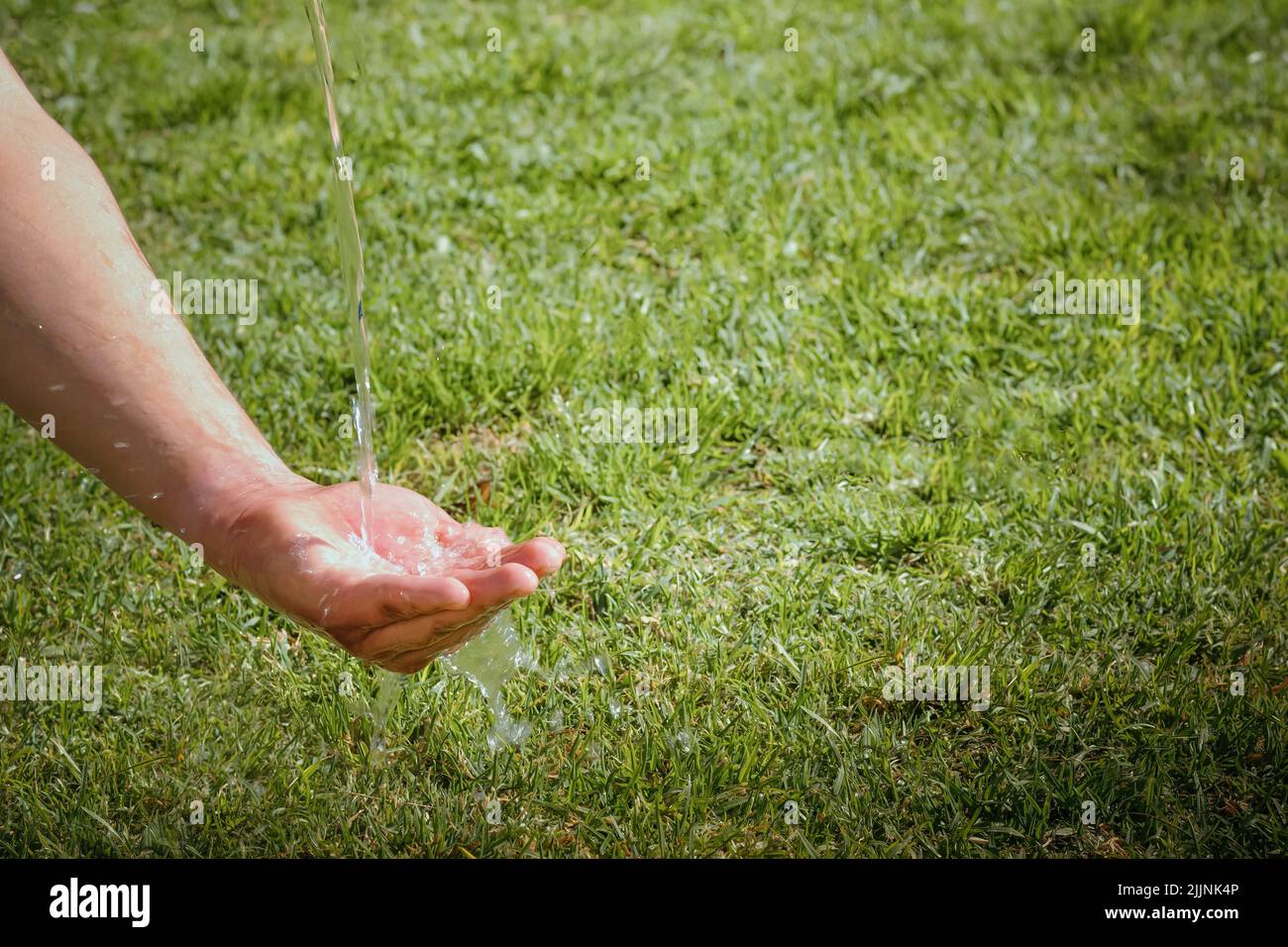 Un primer plano de agua pura vertiendo en una mano con hierba verde en el fondo, espacio de copia Foto de stock