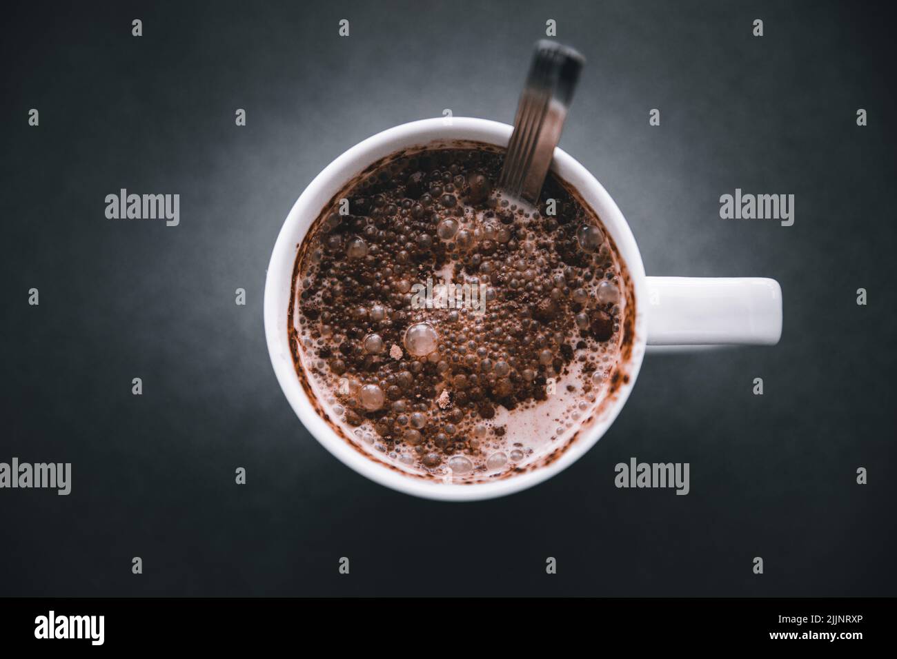 Una taza de chocolate caliente dulce con cacao en polvo sobre la superficie oscura Foto de stock