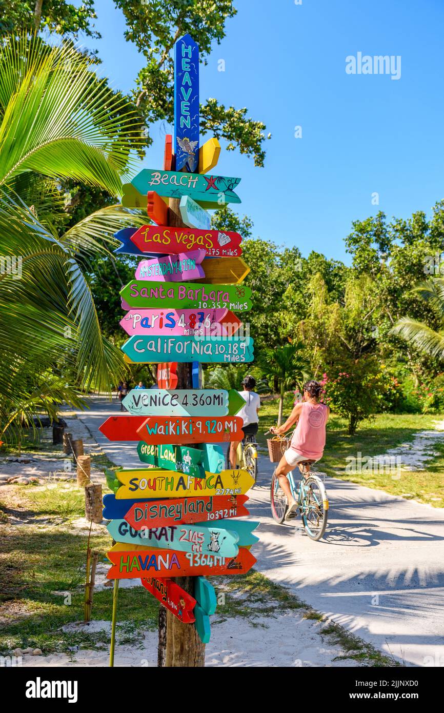 Cartel de colores junto a un carril bici en la isla tropical La Digue en seychelles. Señales con indicadores a destinos turísticos famosos del mundo. Foto de stock