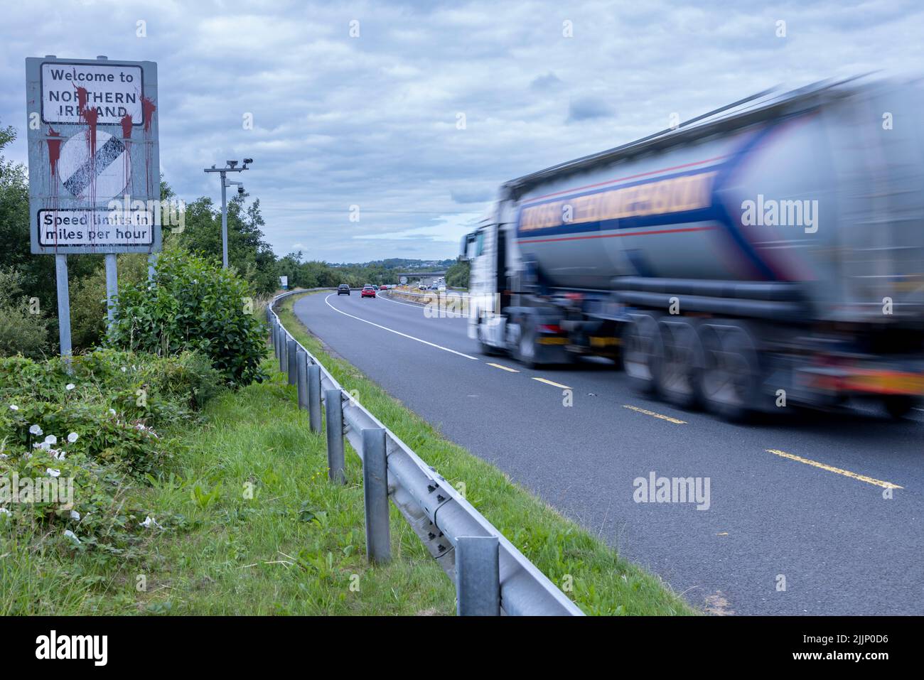 Camión que pasa por la señal de frontera desfigurada entre la República de Irlanda e Irlanda del Norte, Belfast-Dublin Road Foto de stock