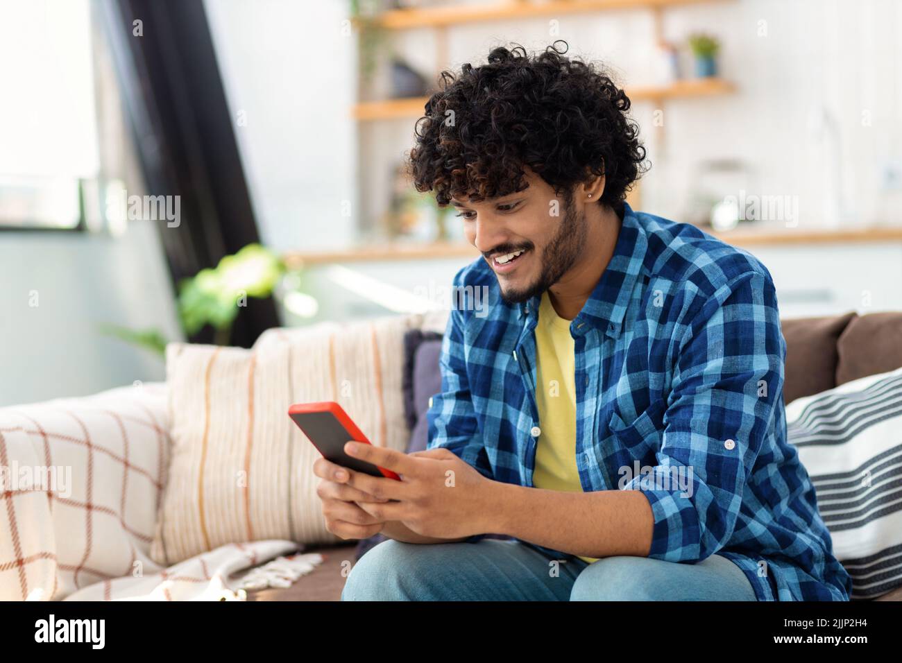 Joven hombre asiático alegre usando teléfono móvil El hombre sostiene el smartphone lee un mensaje, juega juegos Foto de stock