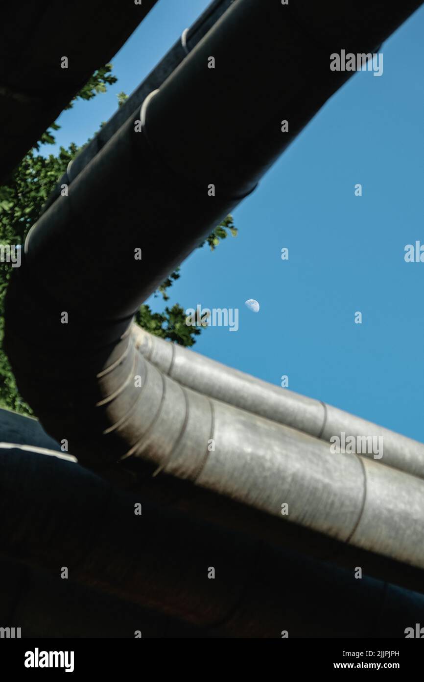 Un plano de ángulo bajo de tubos gruesos de metal con un fondo del cielo azul y la luna Foto de stock