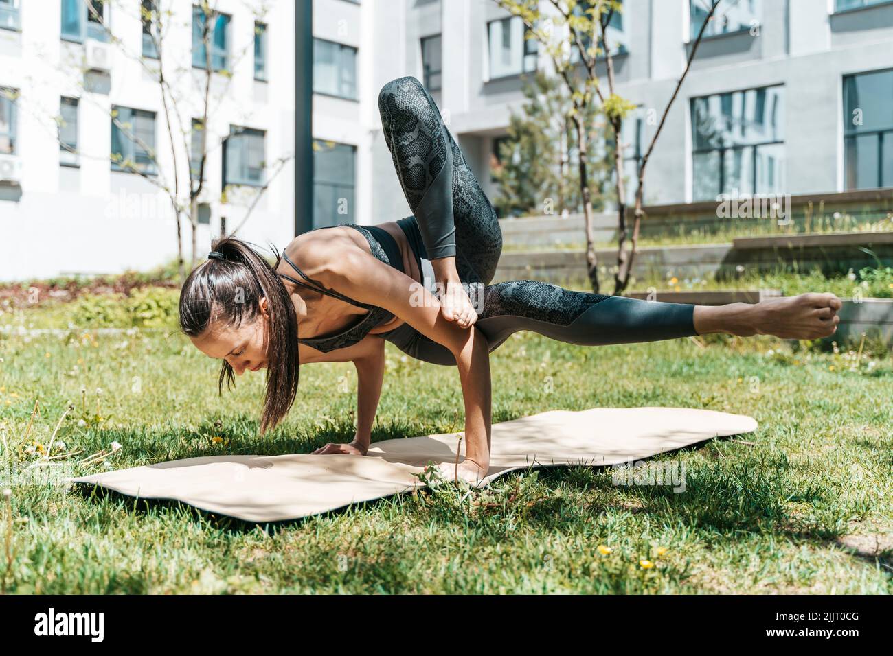 Mujer en yoga pose al aire libre en el parque o jardín. Una chica europea esbelta se dedica al entrenamiento de la práctica del yoga indio para la curación y el desarrollo del cuerpo en el tiempo soleado del verano. Salud, clases, relajación, concepto. Fotografías de alta calidad Foto de stock