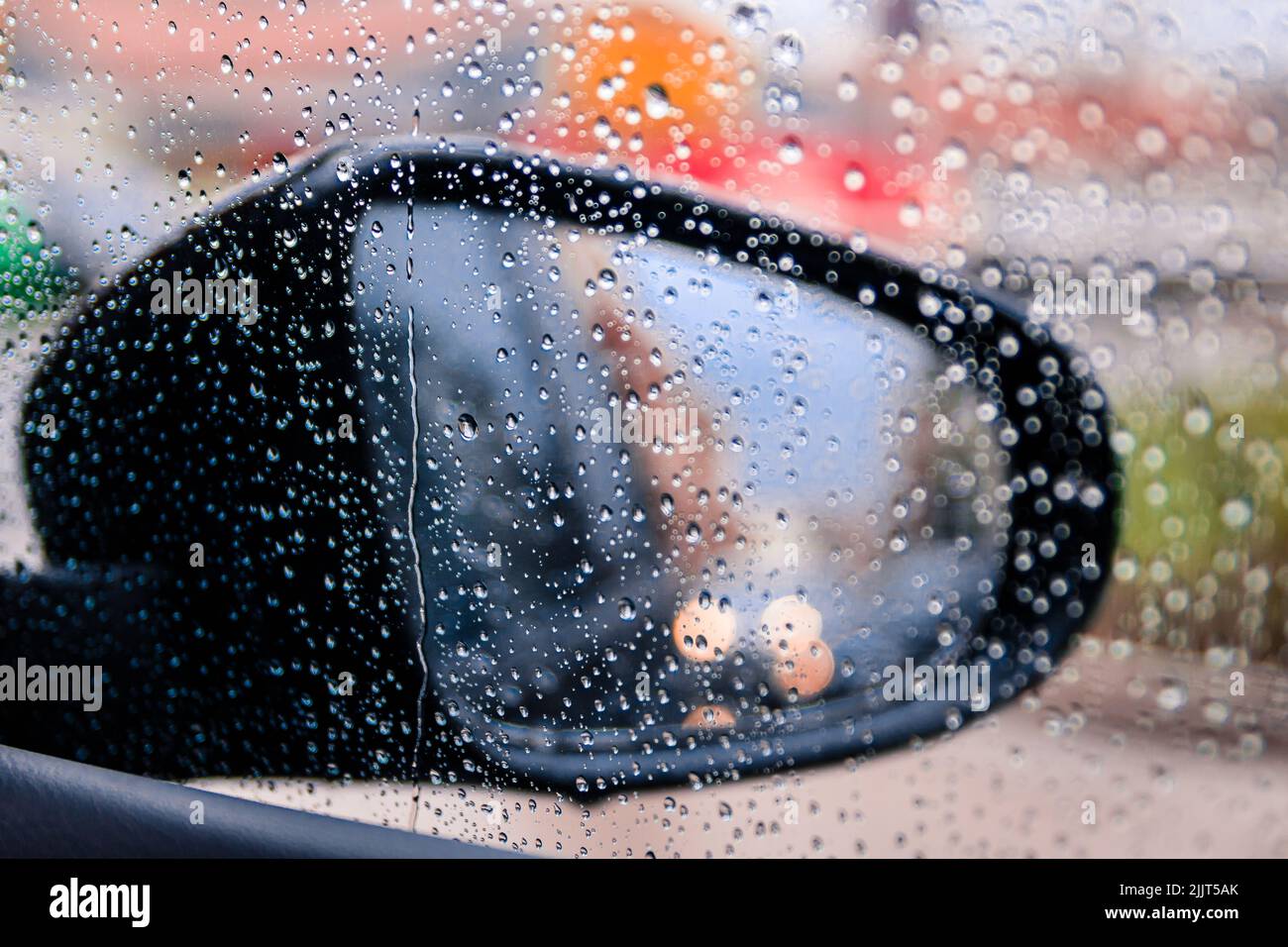 Primer plano de un espejo lateral visto a través del cristal del coche con gotas de lluvia Foto de stock