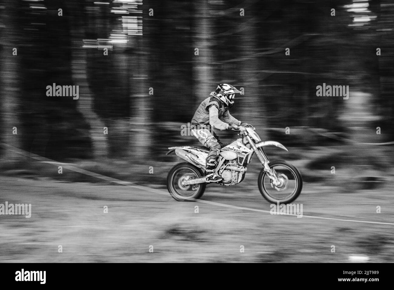 Una fotografía en escala de grises de un motociclista que monta en el bosque durante el motocross Foto de stock