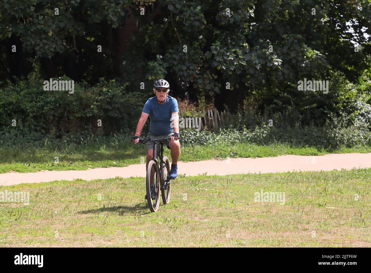 Hombre en sus setenta en bicicleta a caballo a través de Nontake Park Surrey Inglaterra Foto de stock