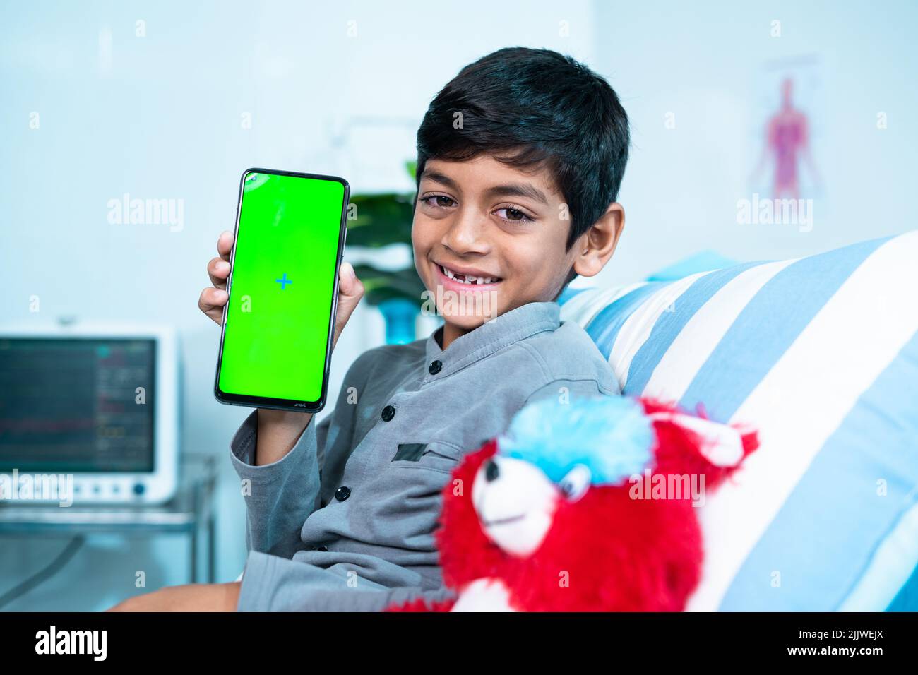 Feliz sonriente se recuperó niño enfermo mostrando teléfono móvil con pantalla verde mientras estaba acostado en la cama en el hospital mirando la cámara - concepto de consultor en línea Foto de stock