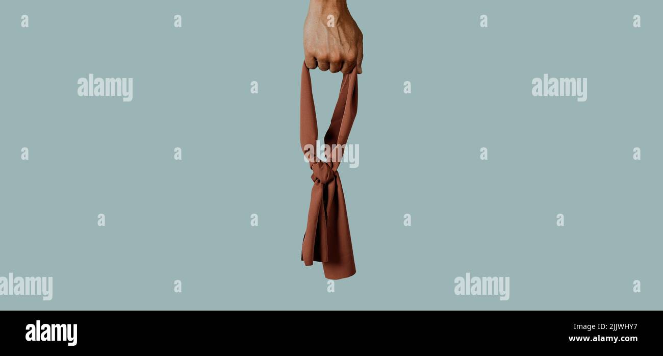 hombre sosteniendo una venda marrón en su mano sobre un fondo gris pálido, jugando con el concepto de que la justicia debe ser ciega, en un formato panorámico para usar Foto de stock
