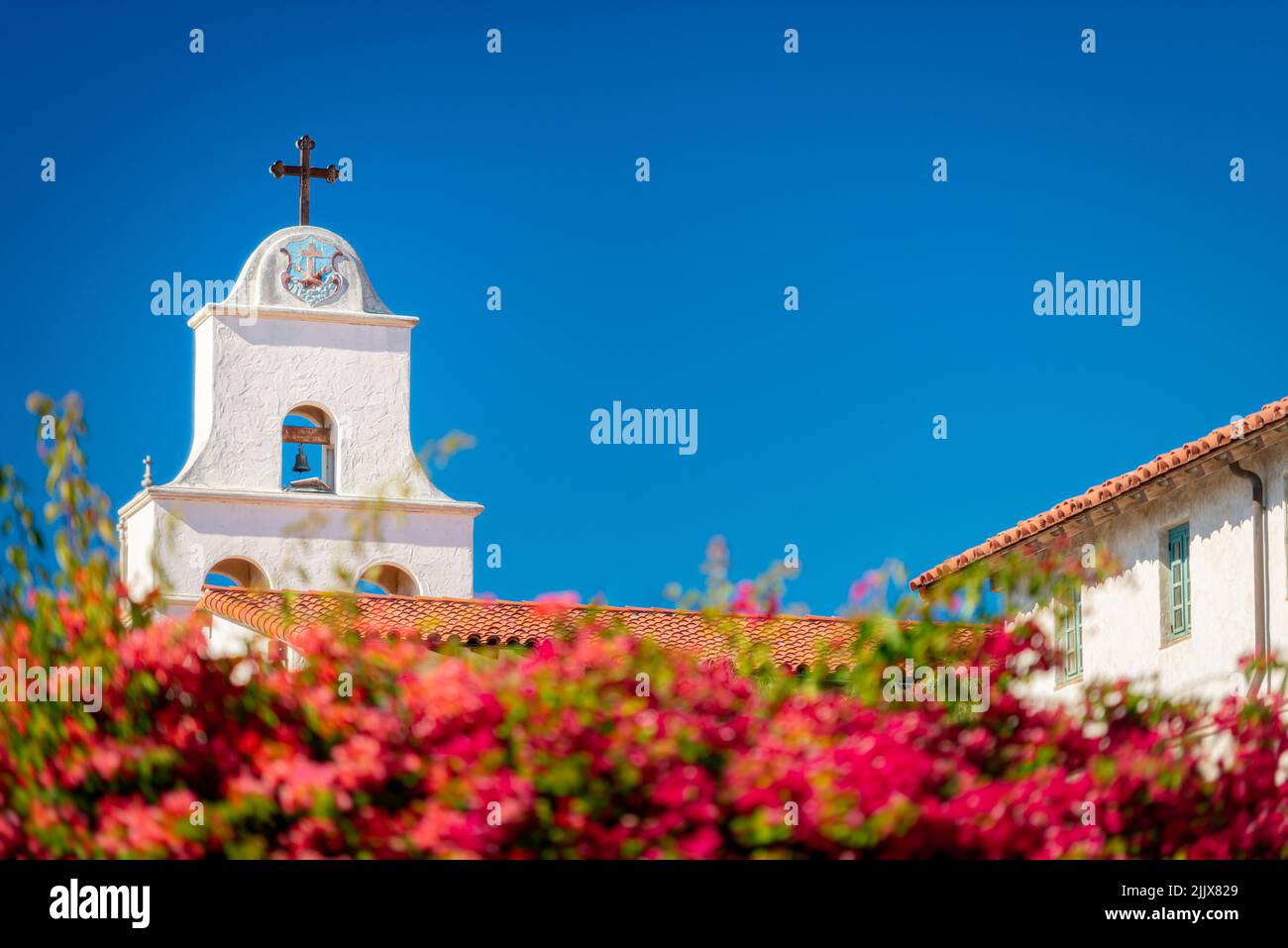 Antigua iglesia en el condado de Santa Bárbara, Estados Unidos de América. Cielo azul en el fondo y flores en primer plano. Foto de stock