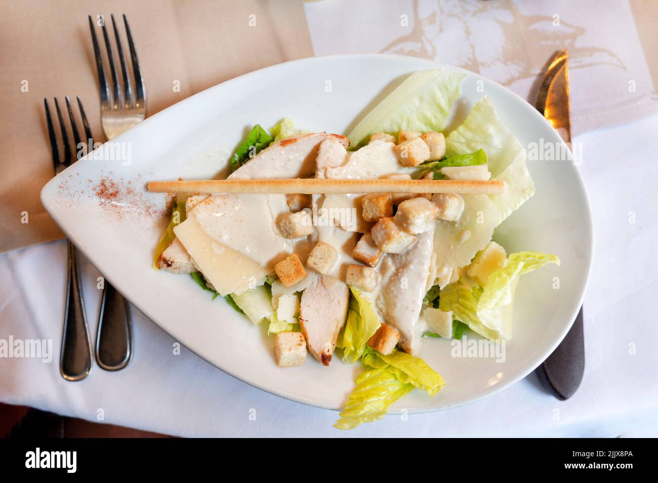 Una ensalada César clásica, bellamente presentada, servida en una mesa del restaurante. La ensalada se remata con una salsa cremosa y picatostes Foto de stock