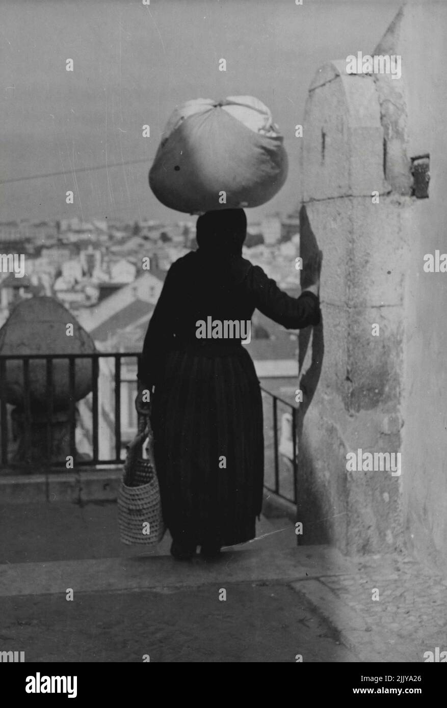 Trabajadoras de Portugal -- ha estado para recoger el lavado sucio de un cliente. Antes de bajar los escalones hasta el lavadero público, se detiene para sentir el bulto de su manojo, y captura un vistazo de los tejados de Lisboa. 30 de septiembre de 1949. (Foto de Steven Henty, Pictorial Press). Foto de stock