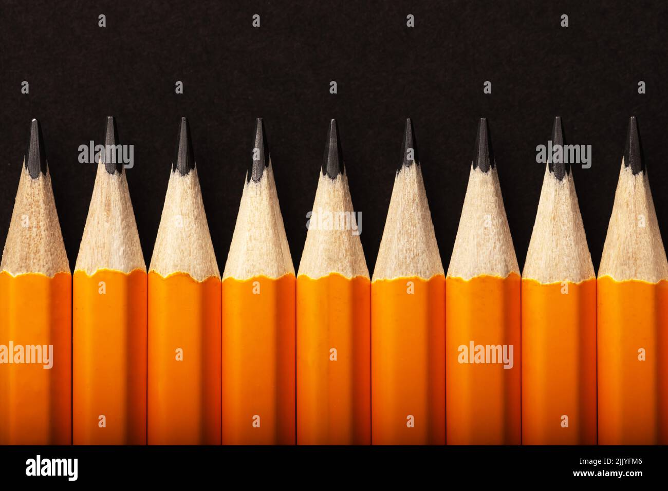Fondo abstracto de lápices de color naranja en una fila sobre fondo negro. Concepto de color Foto de stock