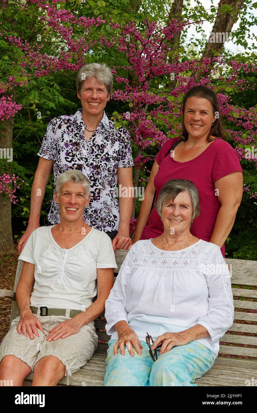 familia, madre mayor, 3 hijas adultas, mujeres, banco de madera, Flores de fondo, árboles, sonriendo, feliz, MR Foto de stock