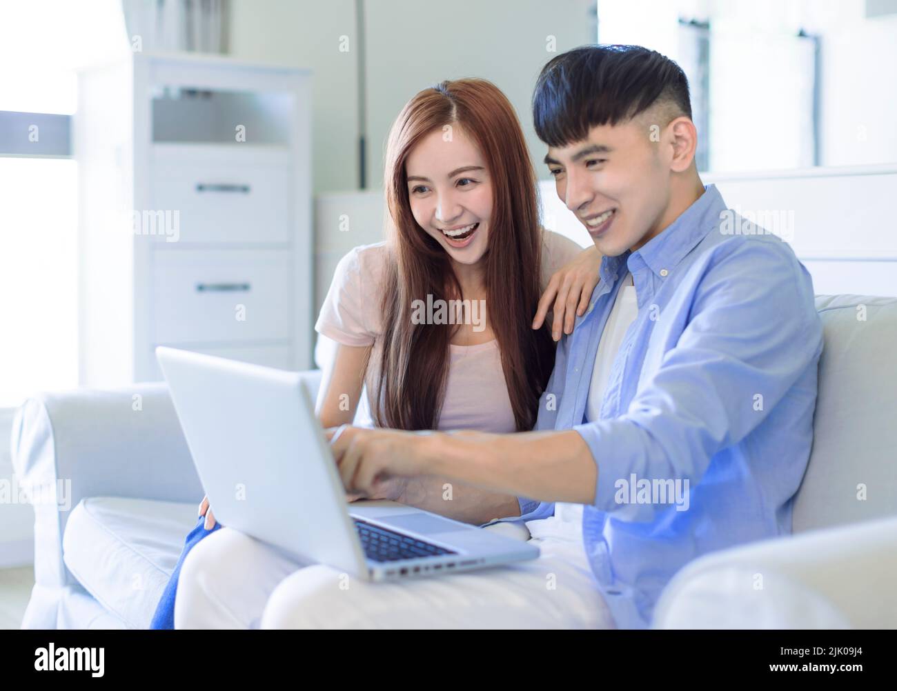 una pareja feliz descansando en un sofá en el salón buscando internet en el ordenador portátil Foto de stock