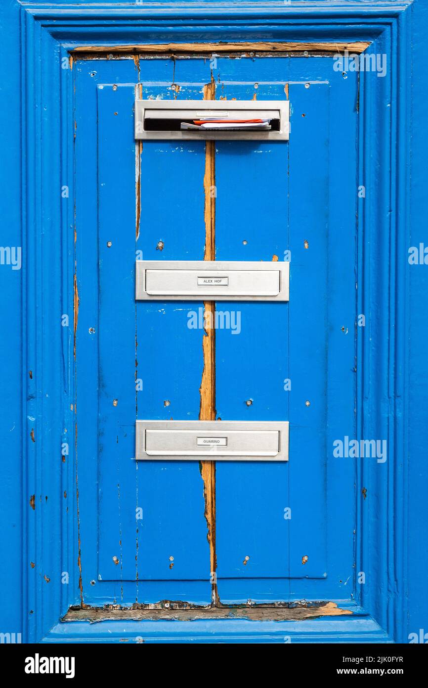 Tres buzones apilados en una puerta azul Foto de stock