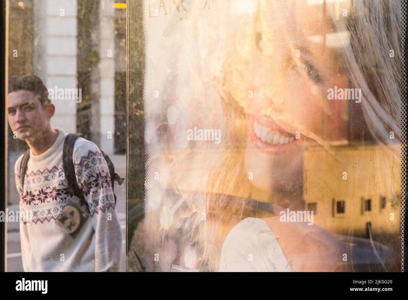 Transeúnte visto a través de un refugio de autobús llevando un cartel publicitario con la cara de Julia Roberts Foto de stock