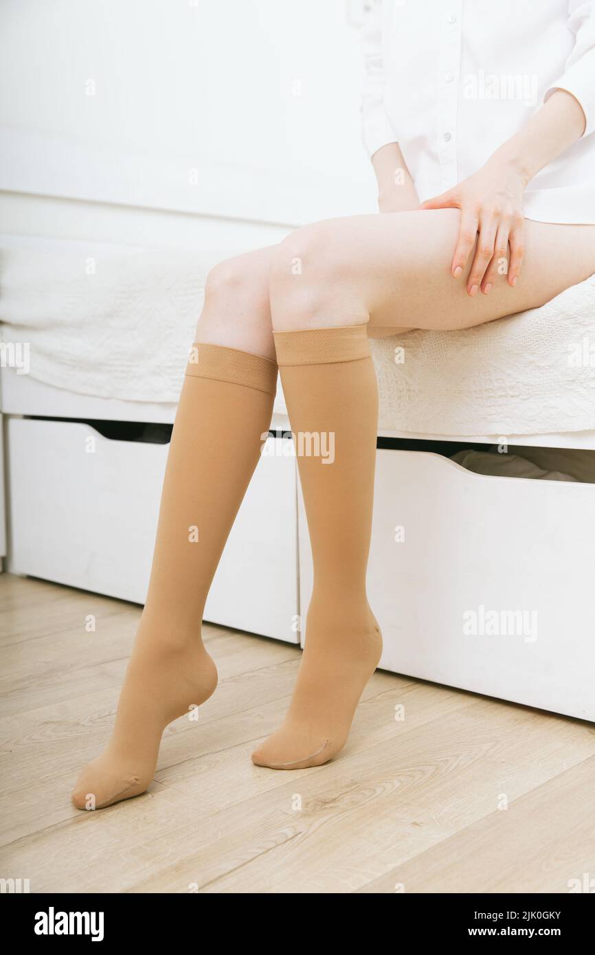 Medias de compresión beige sobre una mujer en una habitación blanca. Calcetines por la rodilla calcetines. Chica poniendo medias en casa. Hermosas piernas femeninas Fotografía de stock - Alamy