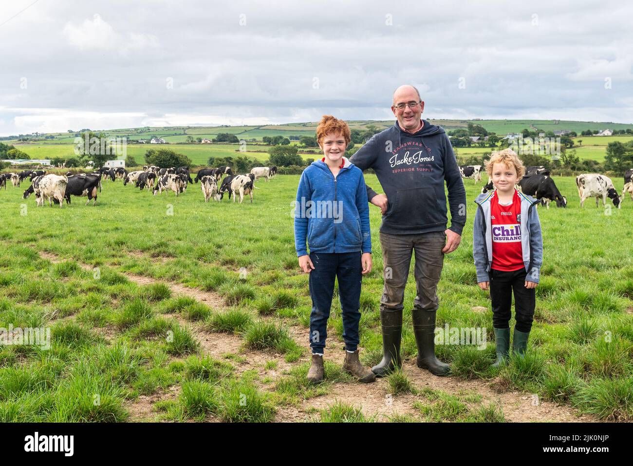 Timoleague, West Cork, Irlanda. 29th de julio de 2022. DJ Keohane, granjero de productos lácteos, cruza su manada de vacas lecheras durante los R600 cerca de Timoleague después de ordeñar, con uno de sus hijos, Daniel, ayudando. Llega cuando el gobierno acordó anoche una reducción del 25% en las emisiones para el sector agrícola. DJ ordeñe 166 vacas en 200 acres.He es fotografiado con sus dos hijos, Daniel y James. Crédito: AG News/Alamy Live News Foto de stock