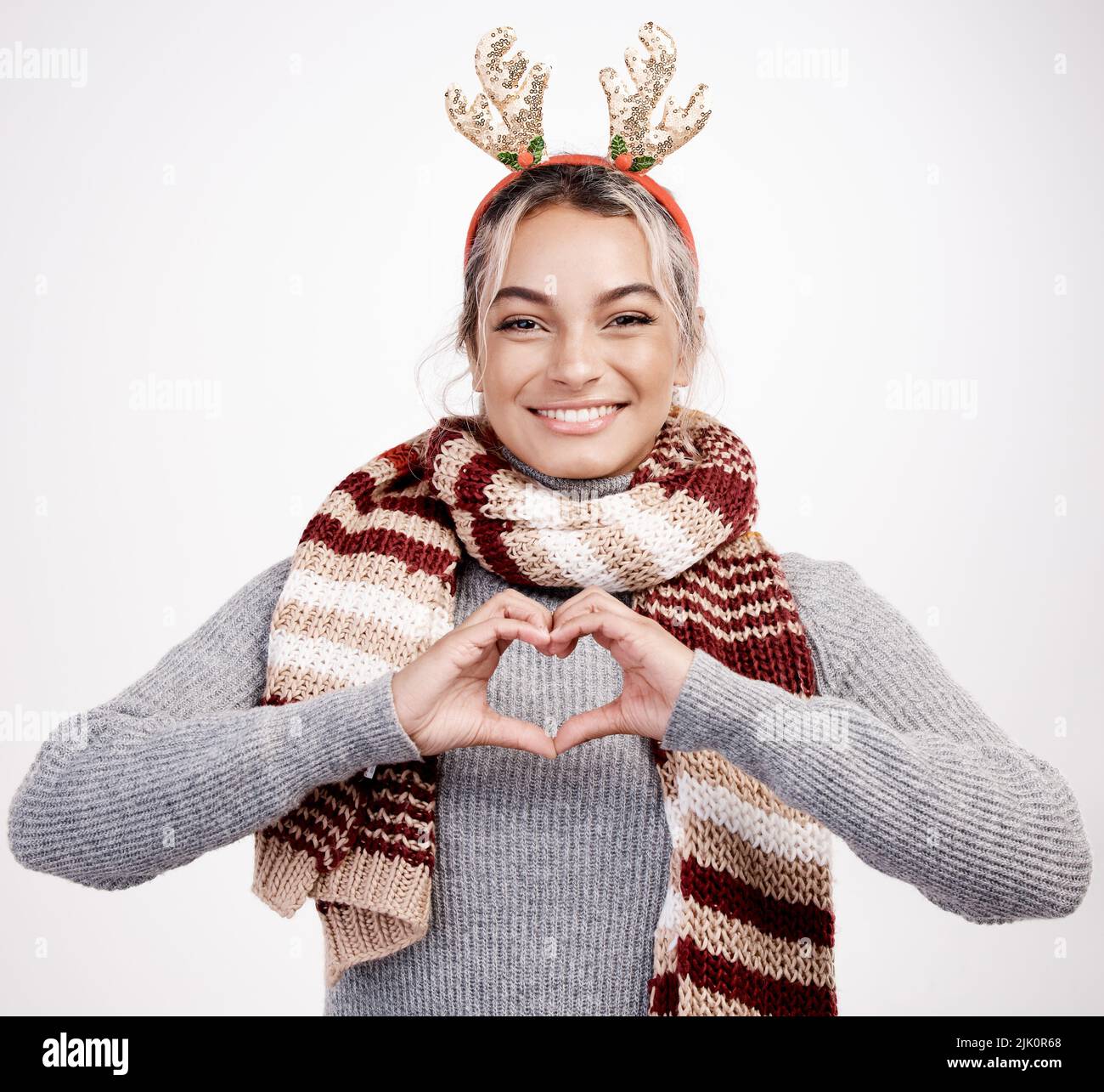 Me encanta la Navidad. Retrato de estudio de una atractiva mujer joven que con las manos se moldea con un corazón vestido con un atuendo de temática navideña. Foto de stock