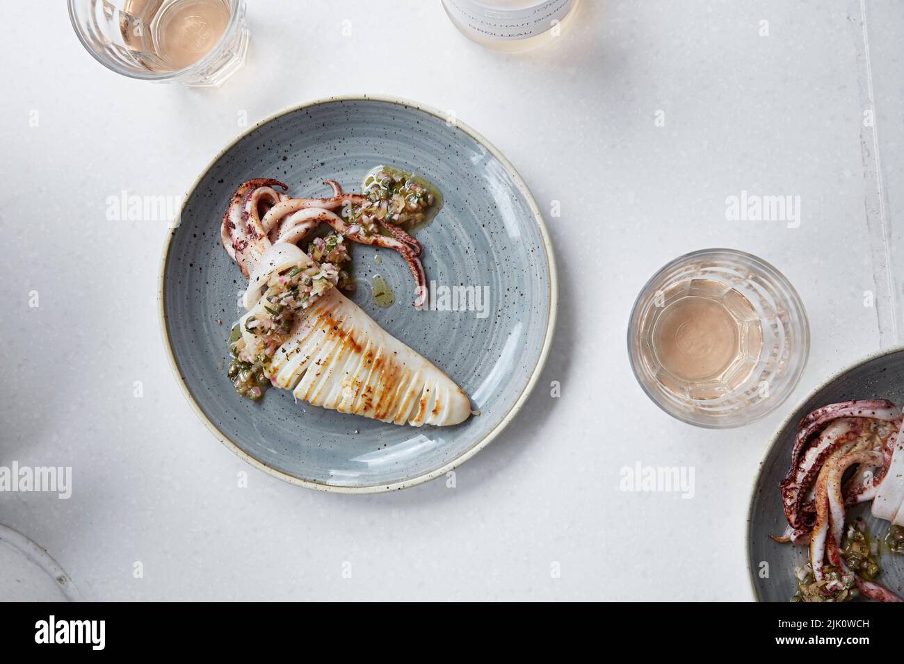 Un elegante plato de calamar servido con un vino rosado ligero Foto de stock