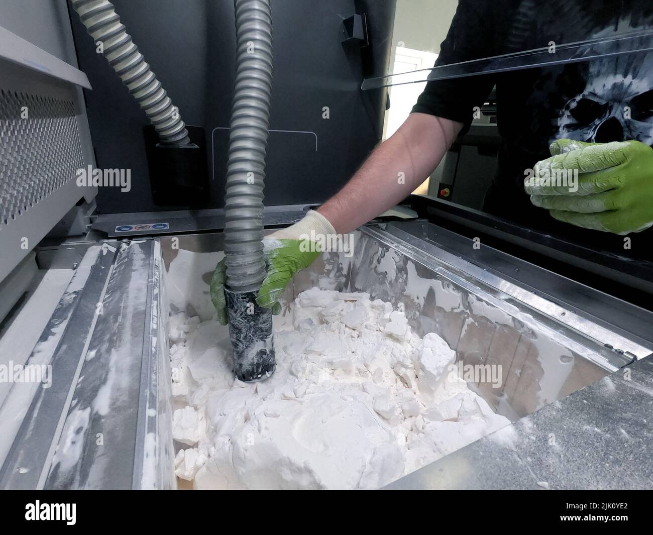 Hombre trabajando con una aspiradora para limpiar el polvo blanco de poliamida de un modelo impreso en una impresora 3D dentro de una impresora 3D. Limpieza de objetos en una impresora