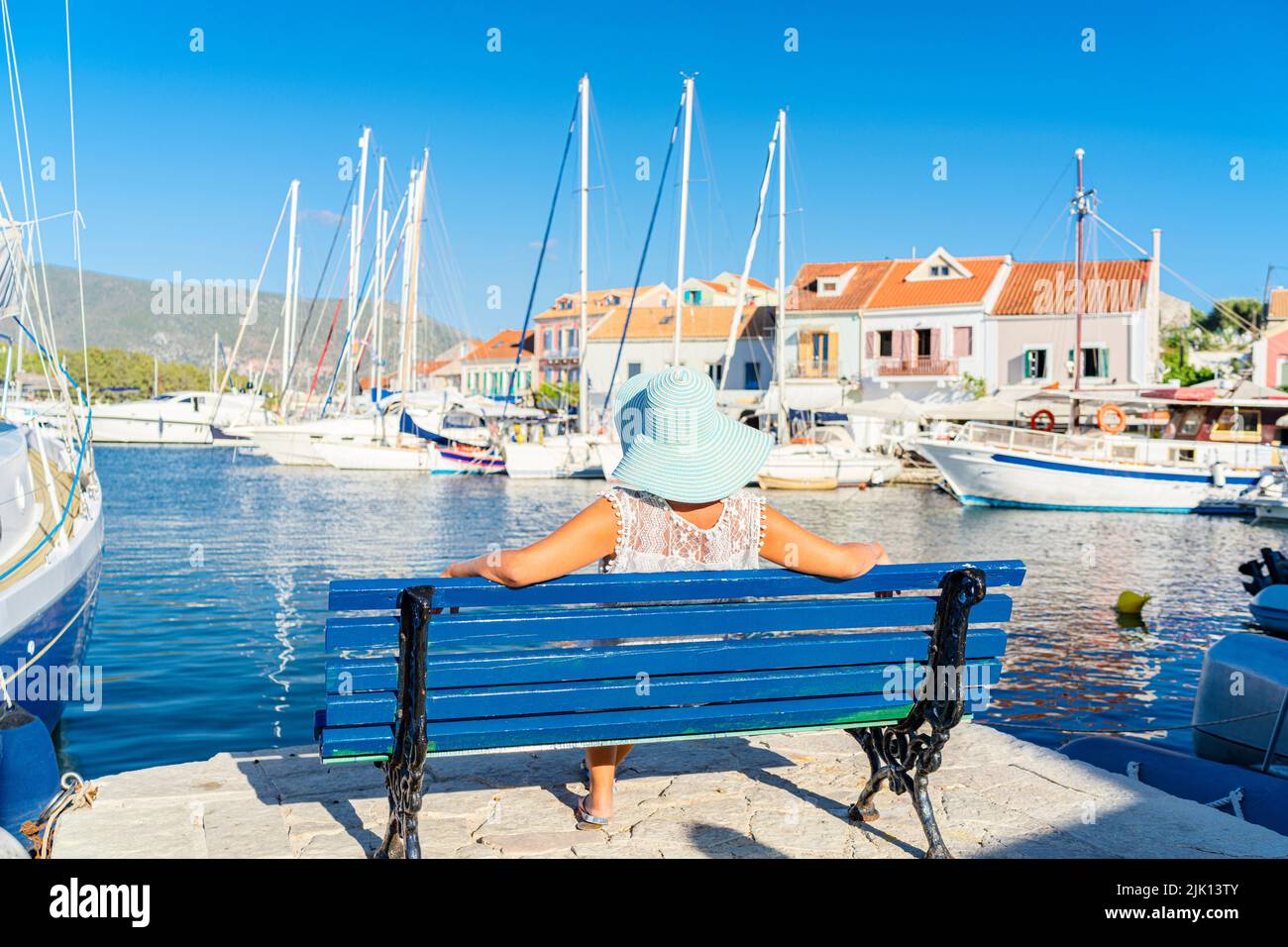 Mujer sin preocupaciones relajándose en un banco en el pequeño puerto de Fiskardo, Cefalonia, Islas Jónicas, Islas Griegas, Grecia, Europa Foto de stock