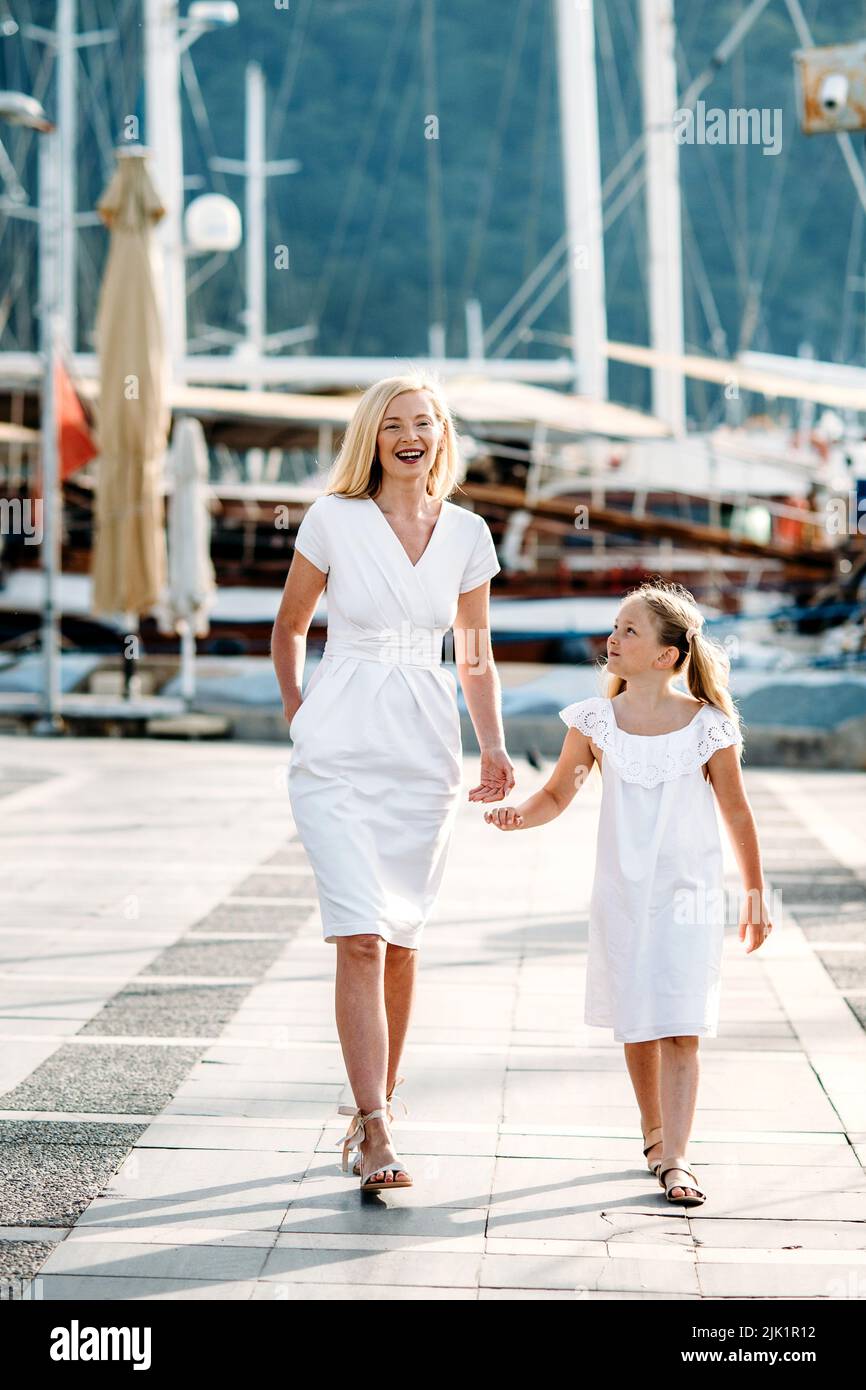 Feliz milenaria madre e hija adolescente rubia con vestidos blancos  caminando por el puerto y el puerto deportivo con yates en un complejo  turístico marítimo Fotografía de stock - Alamy