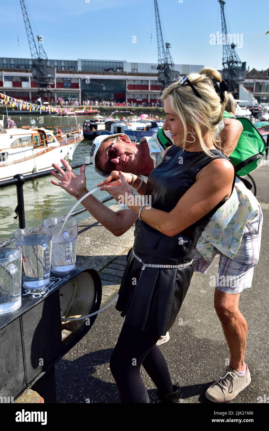 Mujer llenando jarras de agua del grifo mientras un amigo se divierte en el festival del puerto de Bristol, Reino Unido Foto de stock