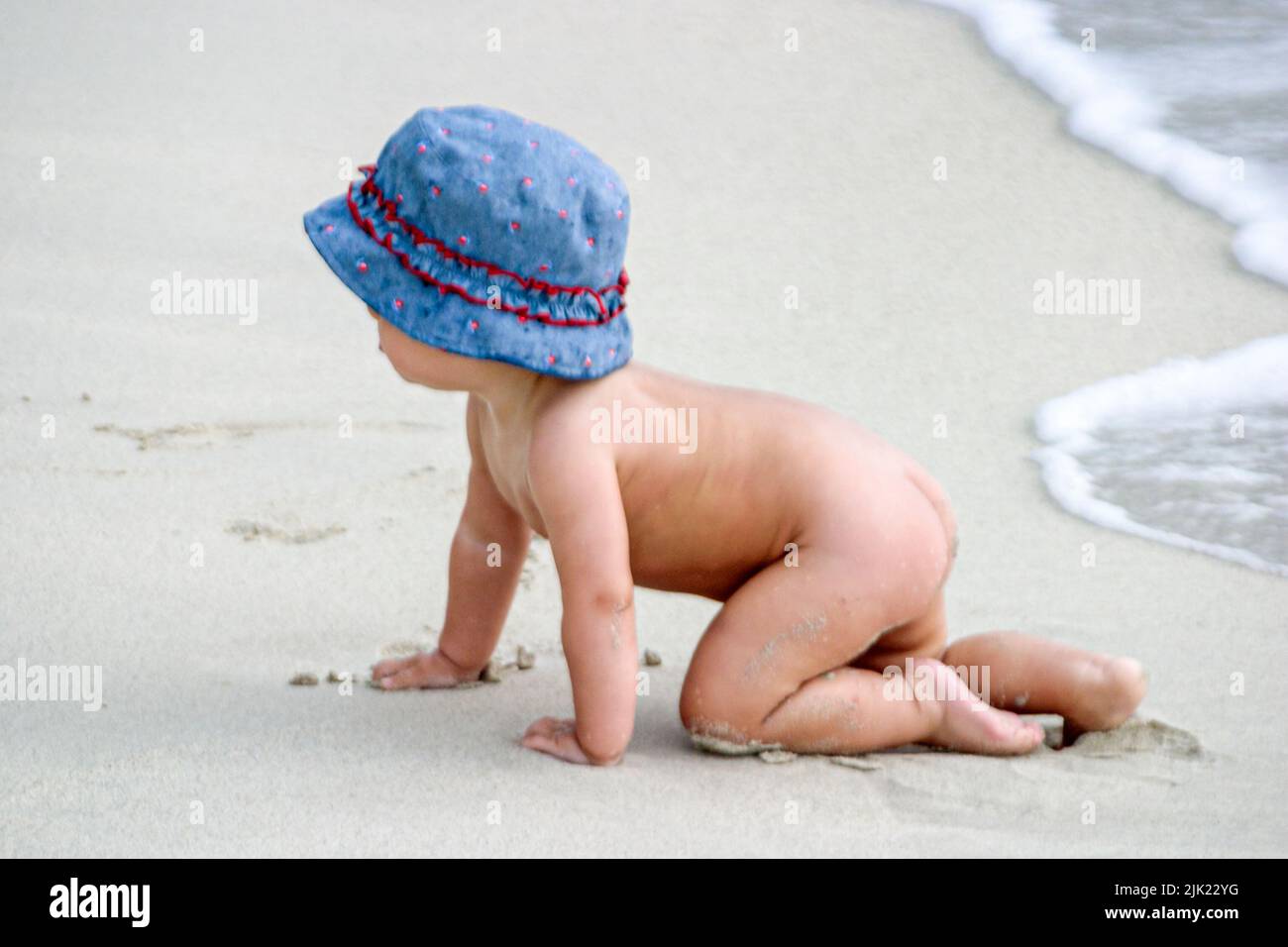 Miami Beach Florida, costa del Océano Atlántico costa costa costa costa costa mar, bebé bebés niño llevar sombrero, gateando cerca de surf desnudo Foto de stock