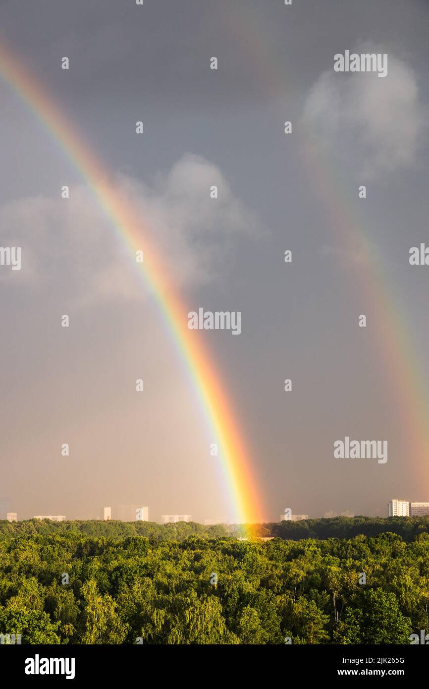 arco iris doble en el cielo azul gris sobre el bosque soleado antes de la tormenta en el soleado día de verano Foto de stock