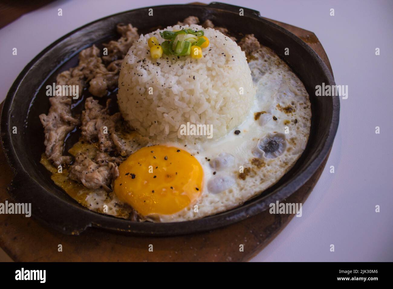 desayuno con arroz, huevo frito y carne o ternera con guarnición de maíz y puerro plato caliente aislado sobre fondo blanco Foto de stock