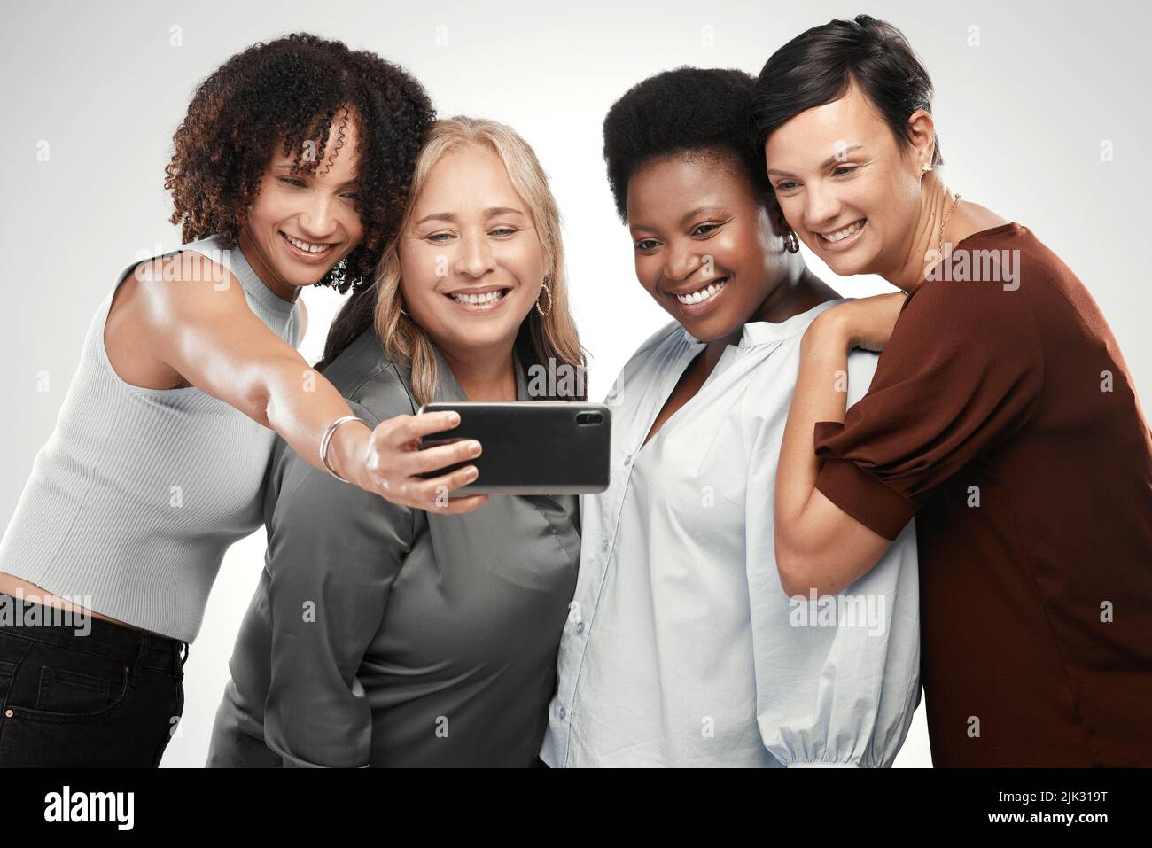 Digamos queso, damas. Un grupo diverso de mujeres que se encuentran juntas en el estudio y toman un selfie con un celular. Foto de stock