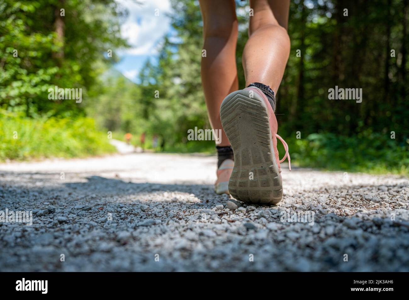 Vista de ángulo bajo de una suela de un zapato de mujer caucásica caminando o caminando por un camino en el bosque. Foto de stock