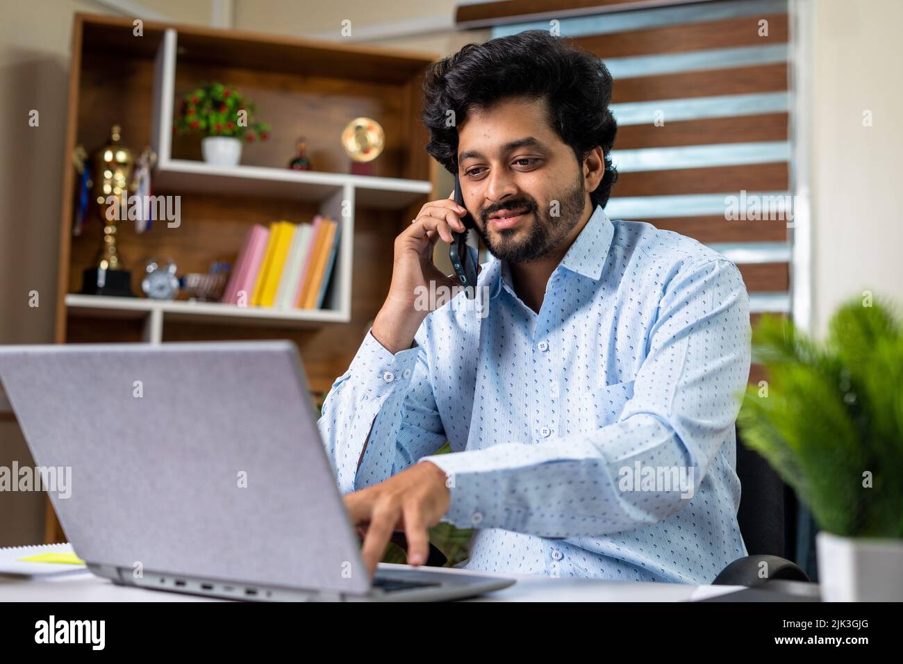 Hombre de negocios feliz hablando con el cliente a través del teléfono móvil mientras trabaja con el ordenador portátil en la oficina: Concepto de consulta, asesor financiero y empleado Foto de stock