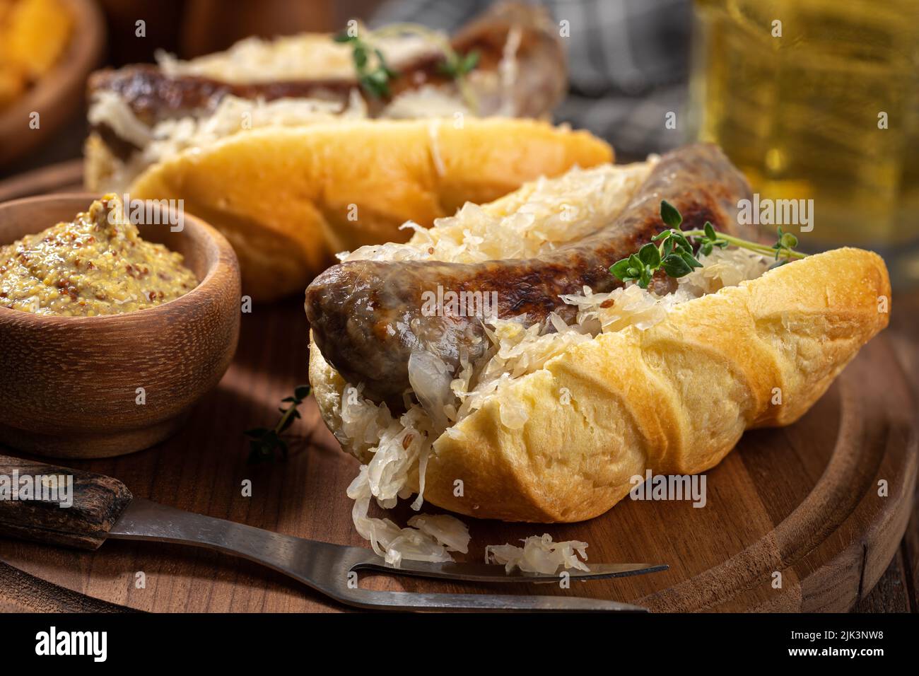 Bratwurst a la parrilla y chucrut en un bollo con mostaza en un tazón sobre una fuente de madera Foto de stock