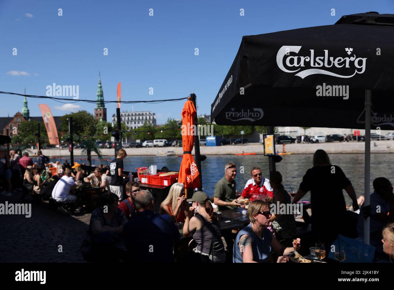 La gente se sienta bajo letreros para la cerveza Carlsberg en una terraza en Copenhague, Dinamarca, 30 de julio de 2022. REUTERS/Andrew Kelly Foto de stock