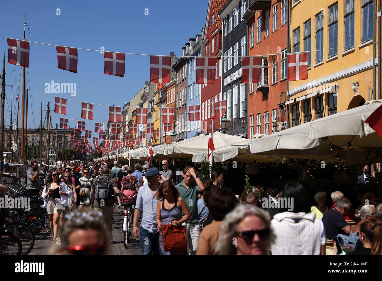 La gente camina mientras se ven banderas danesas colgadas sobre Nyhavn en Copenhague, Dinamarca, 30 de julio de 2022. REUTERS/Andrew Kelly Foto de stock