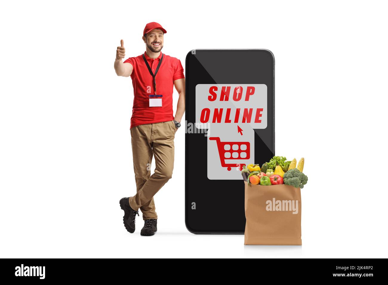 Asistente de tienda masculino con un gran smartphone con tienda de texto en línea y una bolsa de alimentación con pulgares hacia arriba aislados sobre fondo blanco Foto de stock