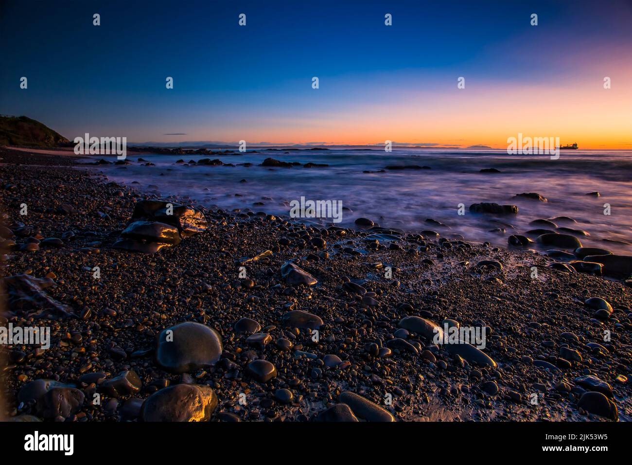 Piedras mojadas guijarros en la playa de guijarros en la ciudad de Forster en Australia, en la costa del Pacífico al amanecer. Foto de stock