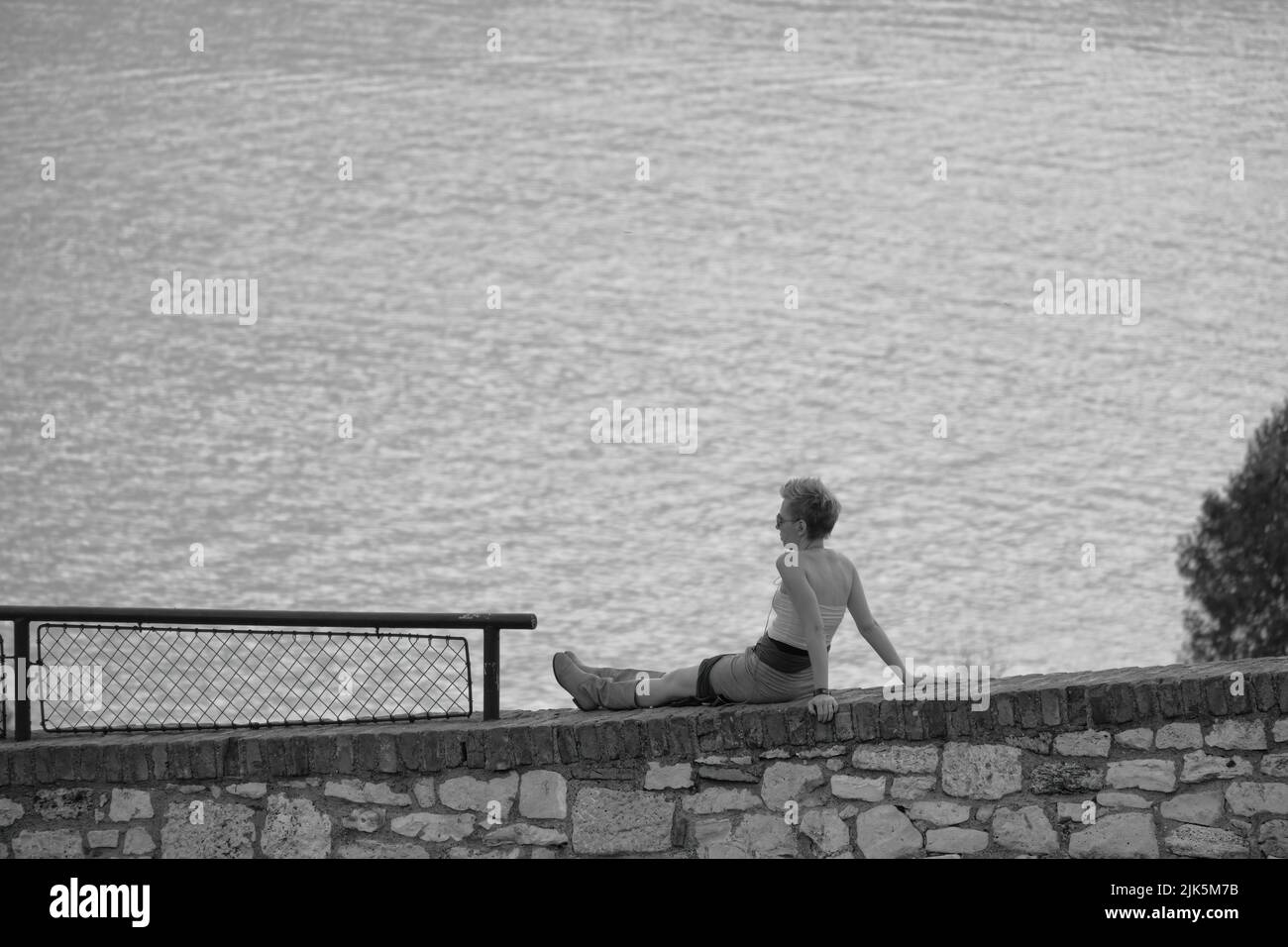 Fotografía en blanco y negro de una mujer joven que se relaja en el parque Kalemegdan de Belgrado, sobre el fondo las aguas del Danubio o la confluencia de los ríos Sava, Serbia Foto de stock