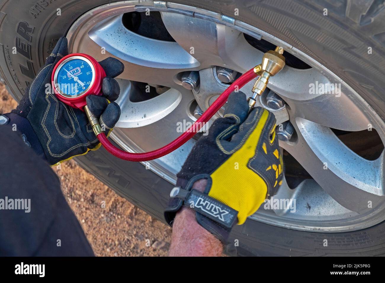 Reducción de la presión en los neumáticos de tracción a las cuatro ruedas con un manómetro de neumáticos para manejar mejor las ondulaciones en carreteras con suciedad Foto de stock