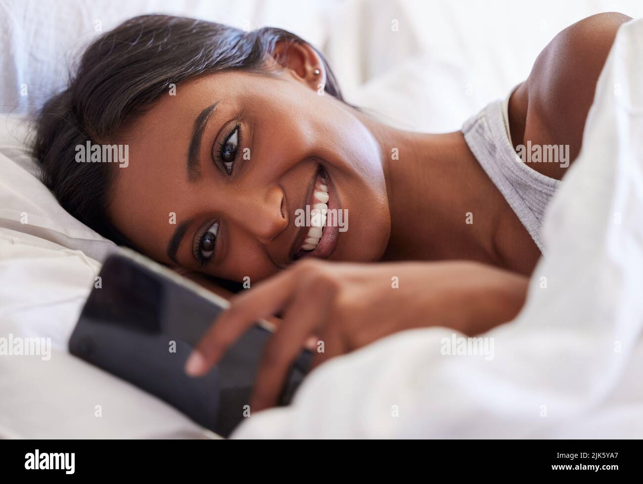 Eso me hizo sonreír. Una joven usando su celular mientras estaba acostada en su cama. Foto de stock