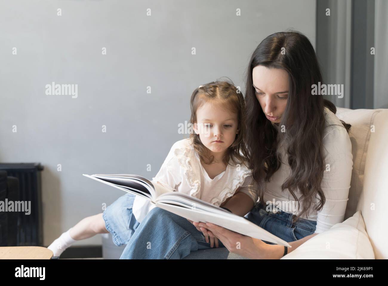 Mamá e hija están leyendo un libro en el sofá. Estudio y actividades con niños en el hogar, desarrollo mental, tiempo libre con niños. Fotografías de alta calidad Foto de stock