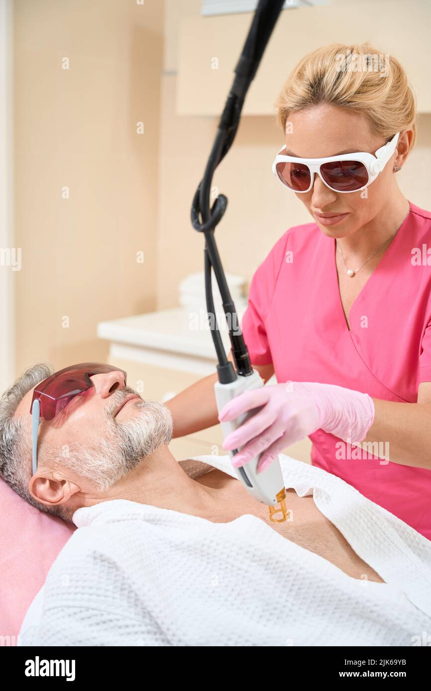 Dermatólogo en gafas realiza la depilación láser en el pecho del