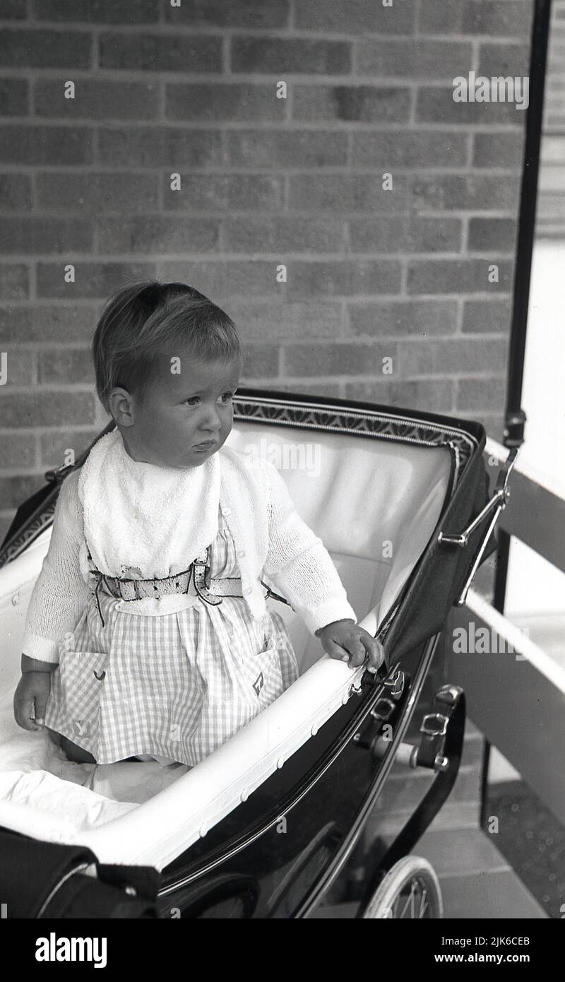 1960s, histórico, atado con un arnés, un niño con aspecto de alma arrodillado en un cochecito tradicional de la época, Inglaterra, Reino Unido. Foto de stock