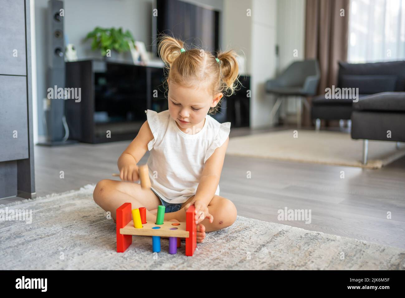 Bonita niña caucásica jugando en el suelo en casa con juguetes de madera ecológicos. Juguete Montessori. El niño jugando juegos educativos. Foto de stock