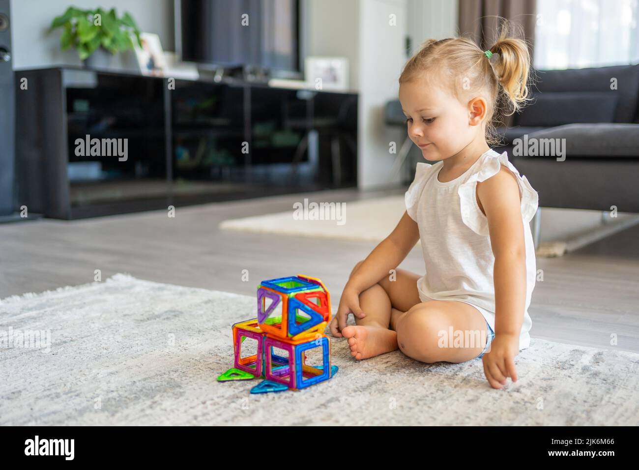 Pequeña niña jugando a bloques de plástico imán colorido kit en casa. El niño juega juegos educativos. Desarrollo de la primera infancia. Foto de stock