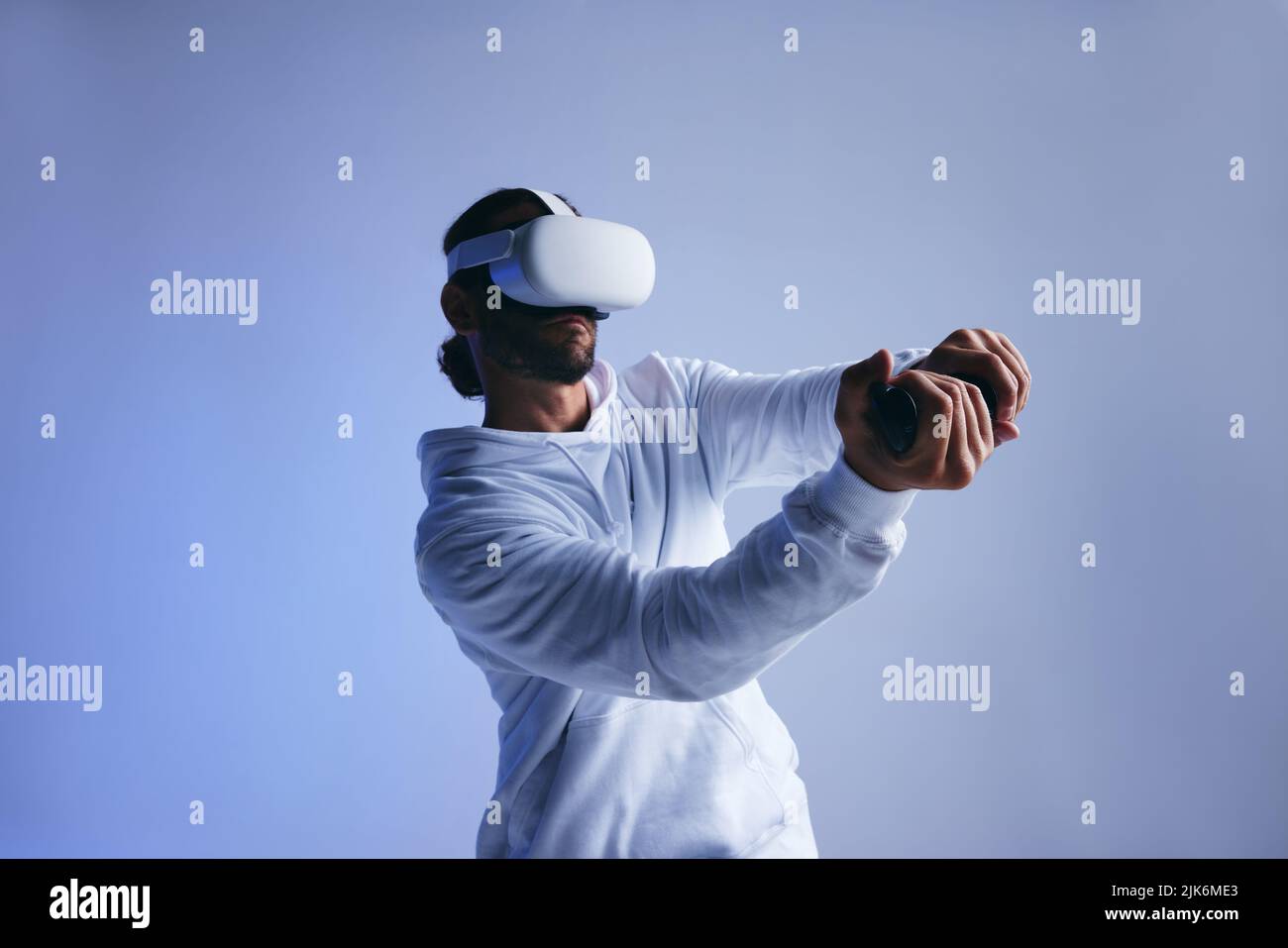 Hombre jugando un juego de cricket en realidad virtual. Joven deportivo bateando una pelota virtual con mandos de juego. Hombre joven activo explorando inmersi Foto de stock